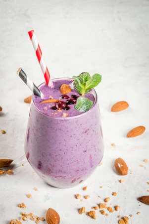 Healthy food. Dietary breakfast, snack. Berry smoothies with granola, black currant, blueberries and nuts almonds, decorated with mint. On a white concrete table with ingredients, copy spaceの写真素材