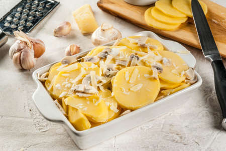 French cuisine. Vegan food. Casserole potato gratin, with ingredients on the background. Unbaked, raw, ready to bake. On a white stone concrete table. Copy spaceの写真素材