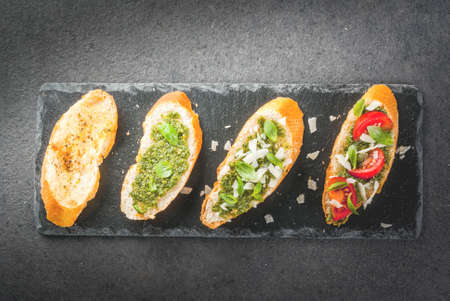 Italian food. Snacks. Antipasto. Bruschetta with pesto sauce, parmesan cheese, cherry tomatoes and fresh basil leaves. On a black stone table, on a slate board.  Top view copy spaceの写真素材