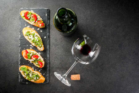 Italian food. Snacks. Antipasto. Bruschetta with pesto sauce, parmesan cheese, tomatoes and fresh basil. On black table, on slate board. With glass of red wine. Top view copy space selective focusの写真素材