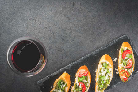 Italian food. Snacks. Antipasto. Bruschetta with pesto sauce, parmesan cheese, tomatoes and fresh basil. On black table, on slate board. With glass of red wine. Copy space selective focusの写真素材