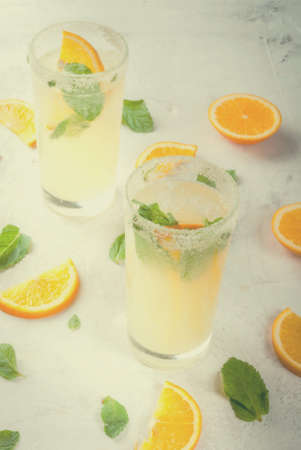 Summer drink. Fresh orange and mint lemonade with ice in glasses, light grey stone marble table,...