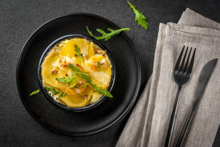 Casserole. French cuisine. Homemade potato gratin in a bowl for baking. On a black stone background. With leaves of fresh arugula for decoration. Top view copy spaceの写真素材