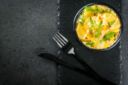 Casserole. French cuisine. Homemade potato gratin in a bowl for baking. On a black stone background. With leaves of fresh arugula for decoration. Top view copy spaceの写真素材
