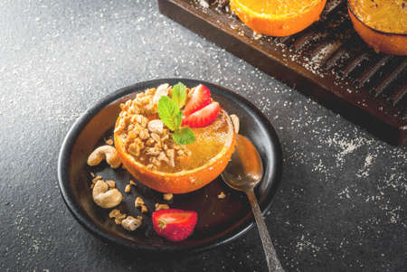 Ideas for a healthy dietary vegan breakfast. Paleo diet. Grilled oranges grapefruits with brown cane sugar, granola, honey, strawberry slices, cashew nuts and mint. On a black stone table. Copy spaceの写真素材