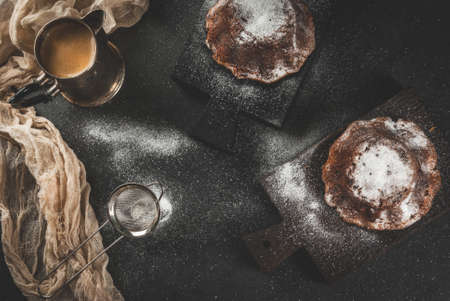 Homemade baking. Country breakfast. Cheese cakes, sprinkled with powdered sugar. On the cutting boards, along with a coffee pot full of coffee. On a black stone table, a low key, copy space top viewの写真素材
