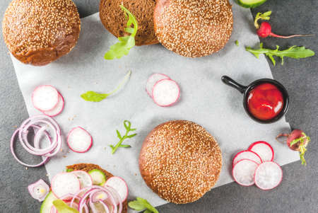 Healthy vegan burgers with beets, carrots, spinach, arugula, cucumber, radish and tomato sauce, whole grain buns on a rustic wooden board on a dark stone background, selective focus, copy space top viewの写真素材