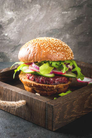 Healthy vegan burgers with beets, carrots, spinach, arugula, cucumber, radish and tomato sauce, whole grain buns on a rustic wooden board on a dark stone background, selective focus, copy spaceの写真素材