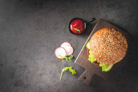 Healthy vegan burgers with beets, carrots, spinach, arugula, cucumber, radish and tomato sauce, whole grain buns on a rustic wooden board on a dark stone background, selective focus, copy spaceの写真素材