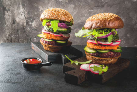 Healthy vegan burgers with beets, carrots, spinach, arugula, cucumber, radish and tomato sauce, whole grain buns on a rustic wooden board on a dark stone background, selective focus, copy spaceの写真素材