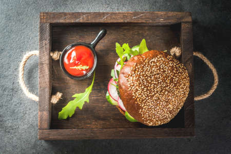 Healthy vegan burgers with beets, carrots, spinach, arugula, cucumber, radish and tomato sauce, whole grain buns on a rustic wooden board on a dark stone background, selective focus, copy space top viewの写真素材