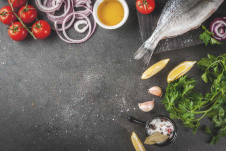 Fresh raw organic fish Dorado, sea bream with ingredients for cooking lemon, tomatoes, onion, salt,...