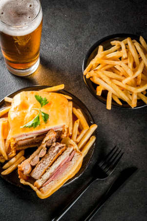 Traditional Portuguese snack food. Francesinha sandwich of bread, cheese, pork, ham, sausages, with tomato beer sauce and French fries. With beer and potatoes. On black table. Copy space top viewの写真素材