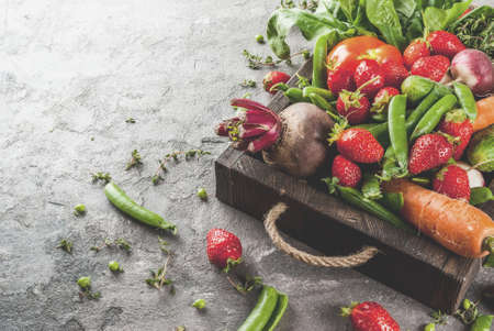 Market. Healthy vegan food. Fresh vegetables, berries, greens and fruits in wooden tray: spinach mint thyme strawberry carrots beets cucumbers radish green peas. On gray table. Copy spaceの写真素材