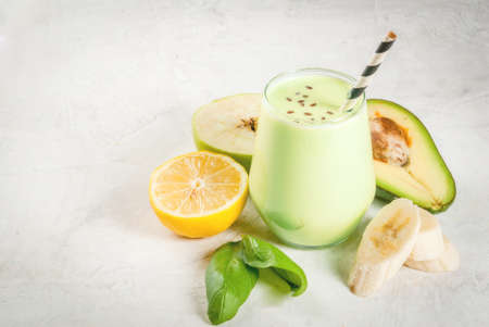 Healthy food. Dietary breakfast or snack. Green smoothies from yoghurt, avocado, banana, apple, spinach and lemon. On white concrete stone table, with ingredients. Copy spaceの写真素材