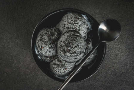 Trendy food. Black ice cream with black sesame, in a black bowl on a black stone table, with a spoon. Copy space top viewの写真素材