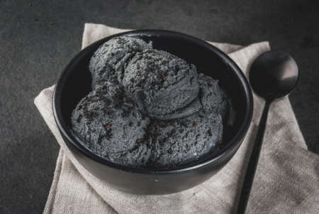 Trendy food. Black ice cream with black sesame, in a black bowl on a black stone table, with a spoon. Copy spaceの写真素材