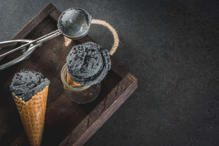 Trendy food. Black ice cream with black sesame, in traditional portioned ice cream cones. On a black stone table, in a wooden tray. Copy spaceの写真素材