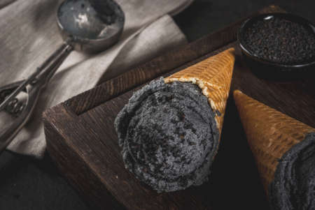 Trendy food. Black ice cream with black sesame, in traditional portioned ice cream cones. On a black stone table, in a wooden tray.の写真素材