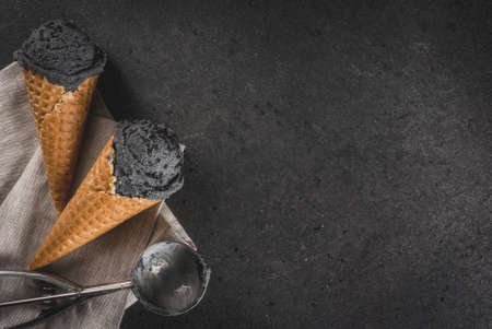 Trendy food. Black ice cream with black sesame, in traditional portioned ice cream cones. On a black stone table, in a wooden tray. Copy space top viewの写真素材