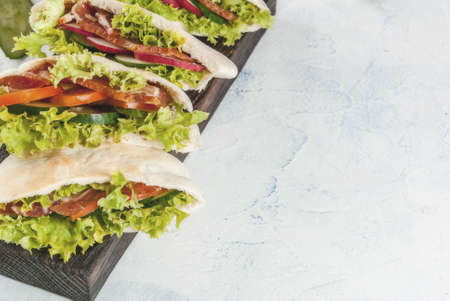 Snack. Takeaway food, street fast food. Pita bread sandwich with fresh vegetables lettuce, cucumber, tomato, radish, beef meat. On a light concrete table on a wooden tray. Copy space top viewの写真素材