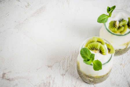Two portions jars of fresh homemade organic Greek yogurt with kiwi puree, pieces of kiwi and mint. On a white stone table, copy spaceの写真素材