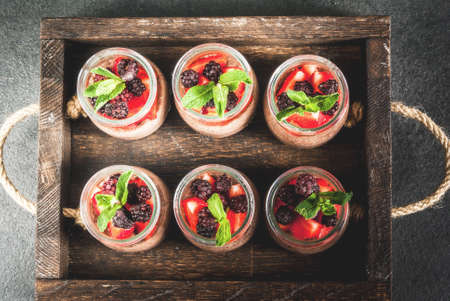 Healthy vegan breakfast. Dessert. Alternative food. Pudding with chia seeds, fresh strawberries, blackberries and mint. On a dark stone background, in an old wooden tray. Top viewの写真素材