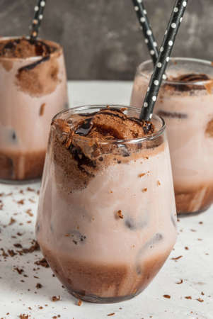 Summer refreshment drinks. Chilled iced chocolate cocoa. With scoop of chocolate ice cream, chocolate powder and ice. In glasses, with tubes for drinking. White concrete table. Copy spaceの写真素材