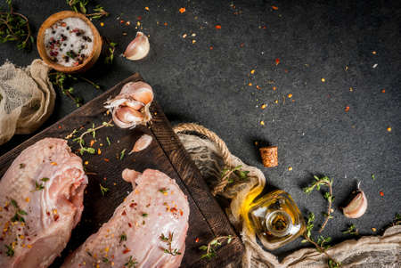 Preparation of food, lunch. Meat. Chicken fillet with skin, raw. On a cutting board, with spices, thyme, garlic, olive oil, salt, pepper. Wooden board, black stone background. Copy space top viewの写真素材