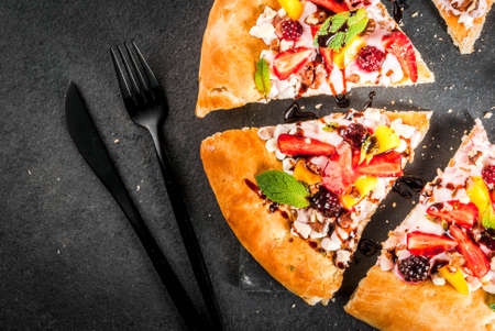 Summer snacks. Food for party. Fruit pizza with cream, currants, yogurt, strawberries, mango, peaches, bananas, blackberries, chocolate, walnuts, mint. On black table. Copy space top viewの写真素材