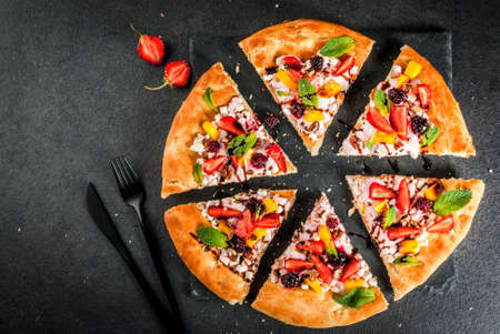 Summer snacks. Food for party. Fruit pizza with cream, currants, yogurt, strawberries, mango, peaches, bananas, blackberries, chocolate, walnuts, mint. On black table. Copy space top viewの写真素材