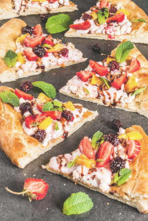 Summer snacks. Food for party. Fruit pizza with cream, currants, yogurt, strawberries, mango, peaches, bananas, blackberries, chocolate, walnuts, mint. On black table. Copy spaceの写真素材