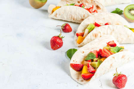 Summer snacks. Food for a party. Fruit tacos with strawberries, mangoes, bananas, chocolate, mint. On a light blue concrete table. Copy spaceの写真素材