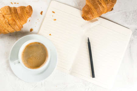 Relaxation. Job. Planning of affairs. White stone table with a notebook for notes, cases, tasks. A cup of fragrant freshly brewed coffee. Freshly baked croissants. Pencil. Copy space top viewの写真素材