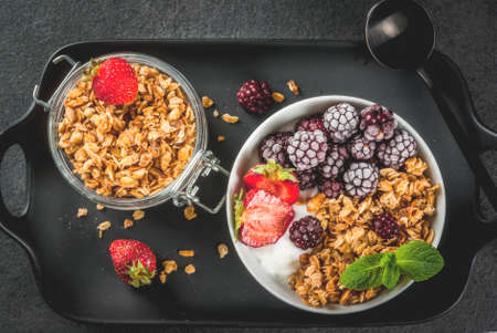 Healthy breakfast. Summer berries and fruits. Homemade Greek yogurt with granola, blackberries, strawberries and mint. On a black stone table, with the ingredients. Top view copy spaceの写真素材