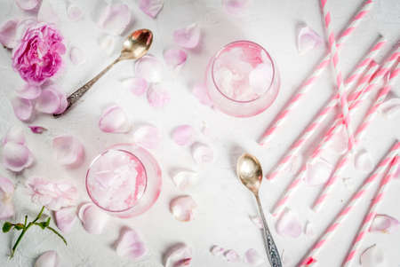 Summer refreshing desserts. Vegan diet food. Ice cream frozen rose, froze, with rose petals and rose wine. White concrete table, with spoons, striped straws, petals and flowers. Copy space top viewの写真素材