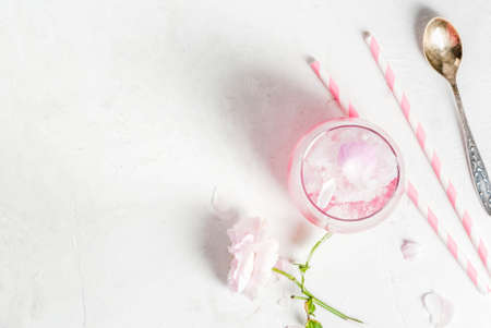 Summer refreshing desserts. Vegan diet food. Ice cream frozen rose, froze, with rose petals and rose wine. White concrete table, with spoons, striped straws, petals and flowers. Copy space top viewの写真素材