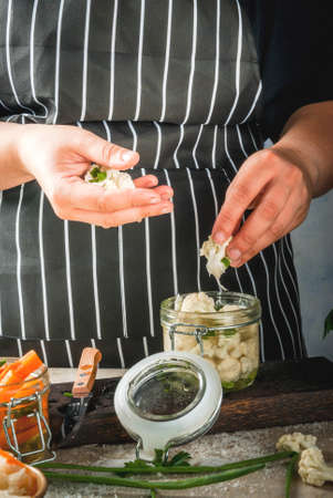 Concept of fermented meal. Canned food. Vegan food. Vegetables. Person (woman) cook fermented sauerkraut salted broccoli cauliflower. Cans with conservation sauerkraut, carrots, greens, onions.の写真素材