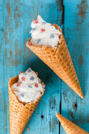Treats for Independence Day holiday on July 4. Homemade cream ice cream in waffles, decorated with stars in traditional colors - blue, red, white. On a blue old wooden table, copy space top viewの写真素材