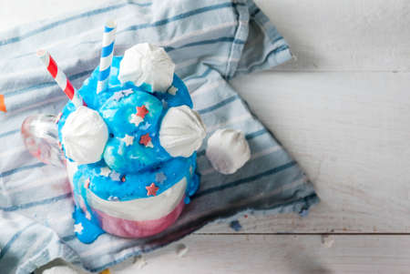 Treats for Independence Day holiday, July 4. Homemade milkshake, crazy shake with ice cream, in traditional colors - blue, red, white, decorated with stars. meringues. On white home table, copy spaceの写真素材
