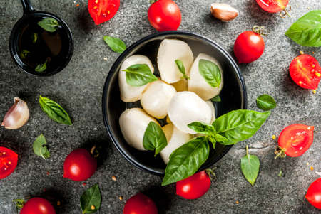 Farm raw organic products. Cooking of dinner in Italian style. Ingredients for caprese salad, pasta, pizza. Basil, tomatoes, mozzarella cheese, olive oil. dark grey stone table. top viewの写真素材