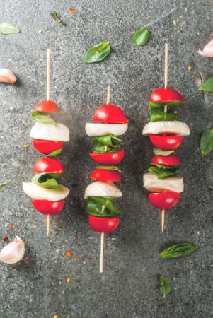 Italian dinner. Homemade salad caprese - tomatoes, fresh basil, mozzarella cheese, olive oil. On a black stone table. Served on skewers. Copy space top viewの写真素材