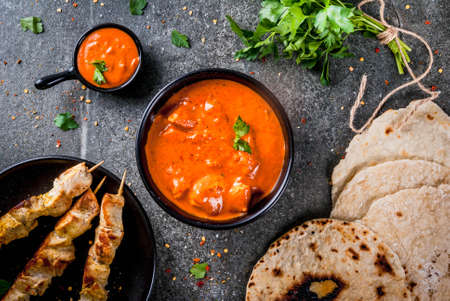 Indian food. Traditional dish spicy chicken tikka masala, butter chicken curry, with indian naan butter bread, spices, herbs. Served in bowl. sauce, on skewers. Stone dark table. copy space top viewの写真素材
