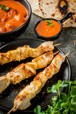 Indian food. Traditional dish spicy chicken tikka masala, butter chicken curry, with indian naan butter bread, spices, herbs. Served in bowl. Sauce, on skewers. Stone dark table. Copy spaceの写真素材