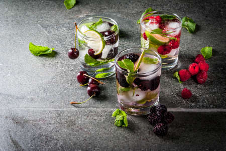 Set of traditional summer refreshing drinks berry mojito. With lime, mint leaves, blackberries, raspberries and cherries. With the ingredients on a dark stone table. Copy spaceの写真素材