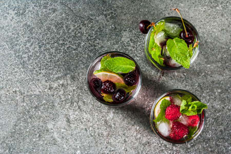 Set of traditional summer refreshing drinks berry mojito. With lime, mint leaves, blackberries, raspberries and cherries. With the ingredients on a dark stone table. Copy space top viewの写真素材