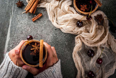 Autumn and winter drinks. Hot cherry  sangria with cinnamon, anise, wine and spices. On a stone dark and wooden background. Girl is holding glass with drink. Female hands in sweater. Top view copy spaceの写真素材