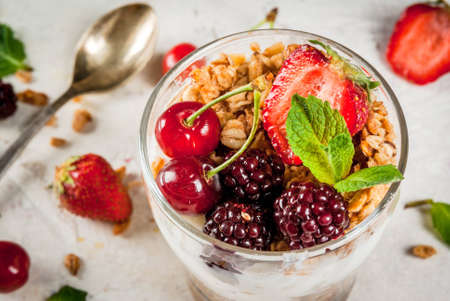 Healthy breakfast. Summer berries and fruits. Homemade Greek yoghurt with granola, blackberries, strawberries, cherries and mint. On white concrete stone table, in glasses. Copy space close viewの写真素材