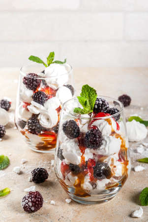 Traditional English dessert. Eton mess - whipped cream, meringue, fresh blackberries, sauce and caramel. In serving glasses on a light stone table. Copy spaceの写真素材