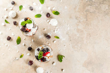 Traditional English dessert. Eton mess - whipped cream, meringue, fresh blackberries, sauce and caramel. In serving glasses on a light stone table. Copy space top viewの写真素材